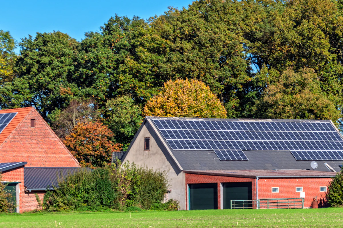 Rooftop solar panels on farm outbuildings beside a green field