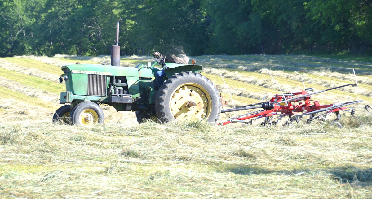 A tractor raking hay across a freshly cut central Indiana field