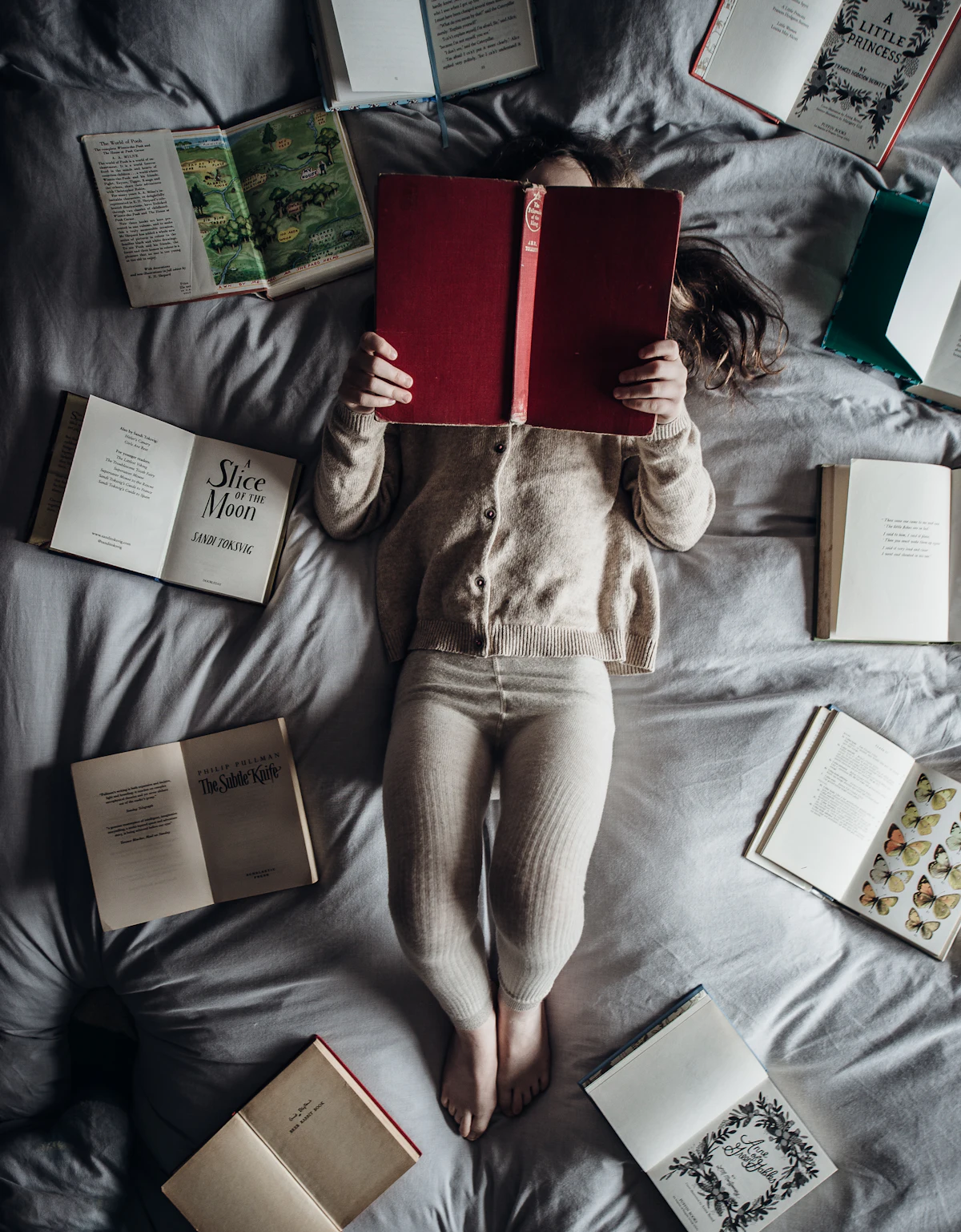 A young girl reading a book surrounded by open storybooks